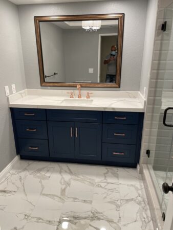 Stylish bathroom remodel, large mirror, bark blue vanity, marble countertop, new tile